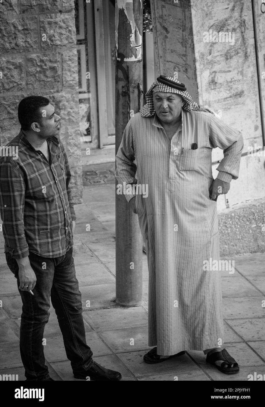 Two men, one in traditional dress and one in western clothing converse on an Amman street. Jordon. Stock Photo