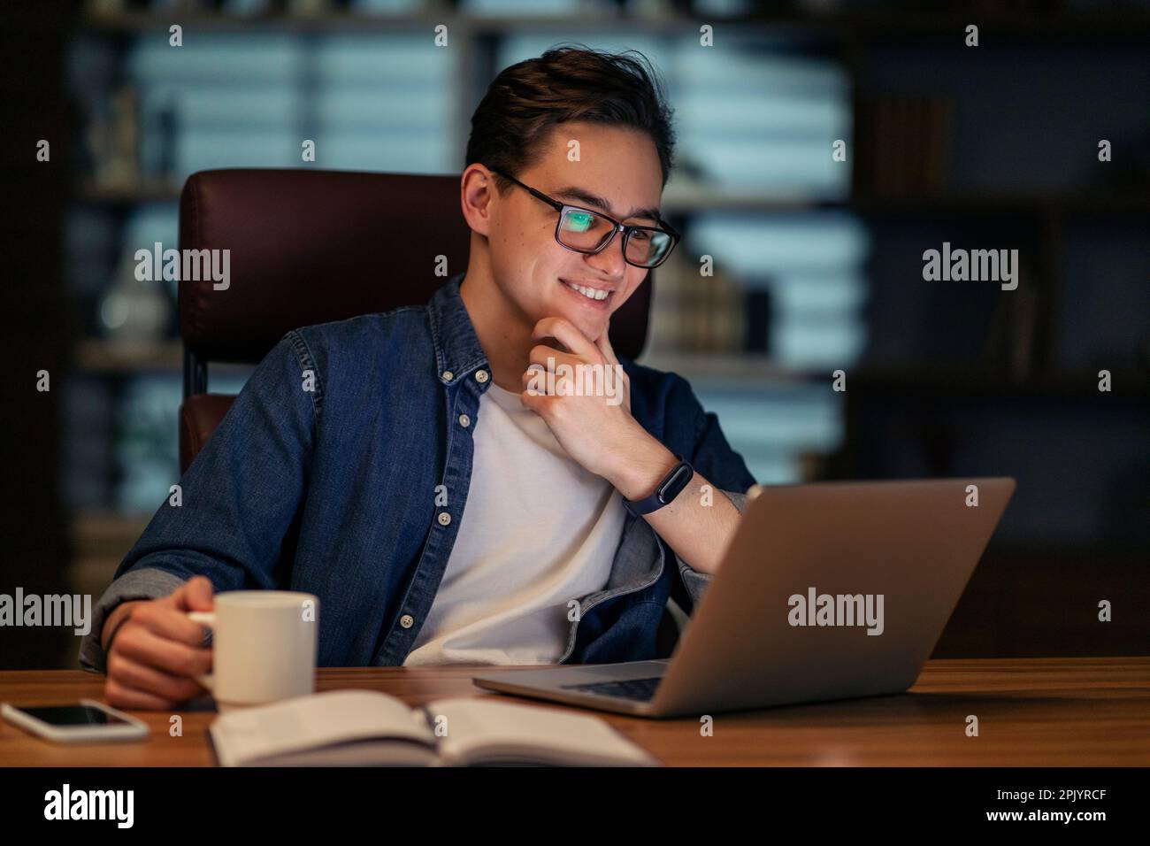 Employee looking at computer screen and smiling, drinking coffee Stock Photo