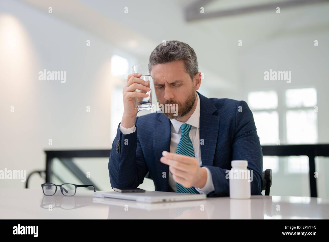 Tired, headache and eye strain from laptop. Businessman with stress, burnout and fatigue eyestrain. Man taking a Medicine pill from headache migraine Stock Photo