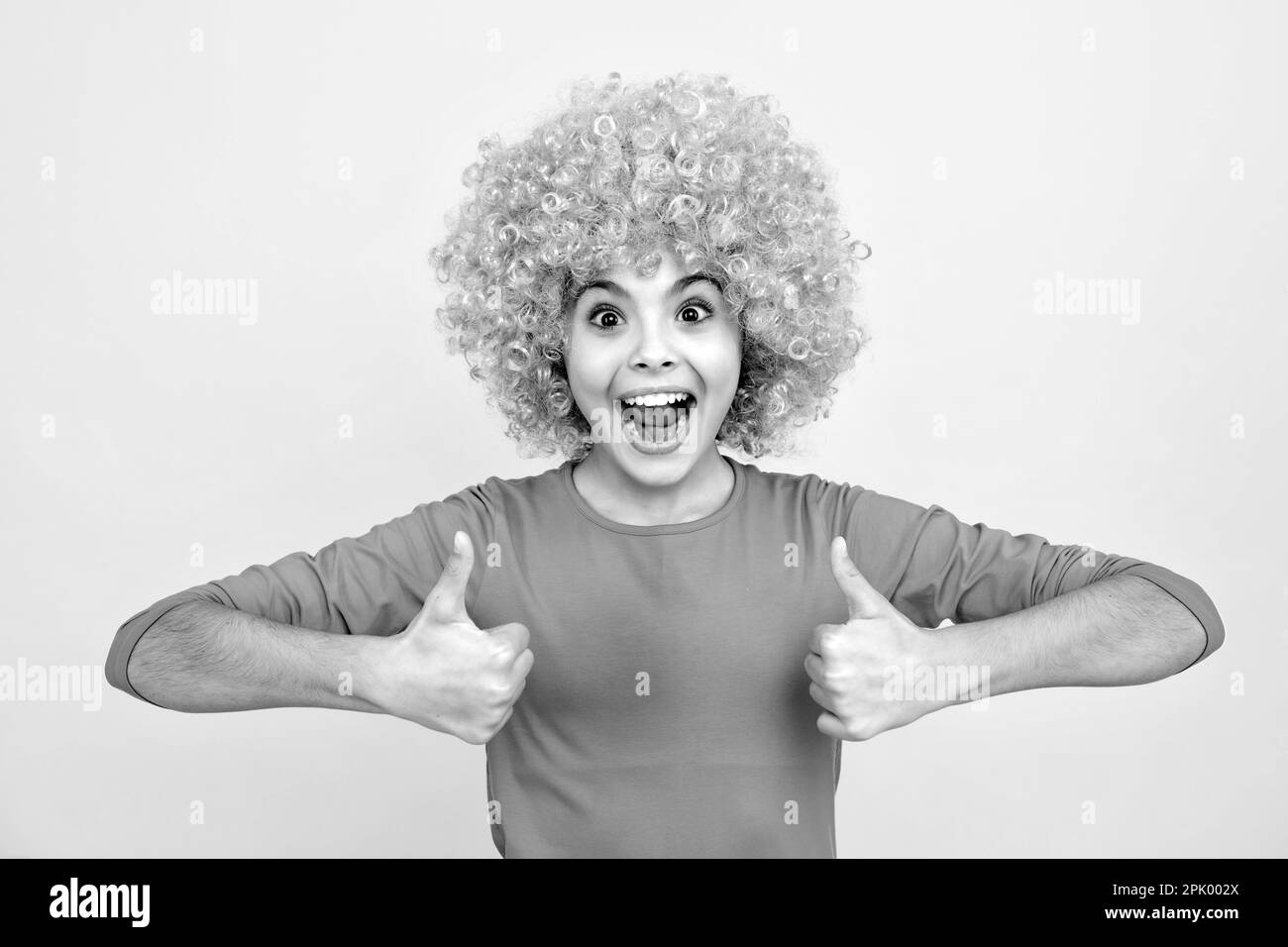 Funny kid with curly hair wig. Cute little girl with fancy hair. Child wearing bright redhead clown hair wig. Excited teenager, glad amazed and overjo Stock Photo