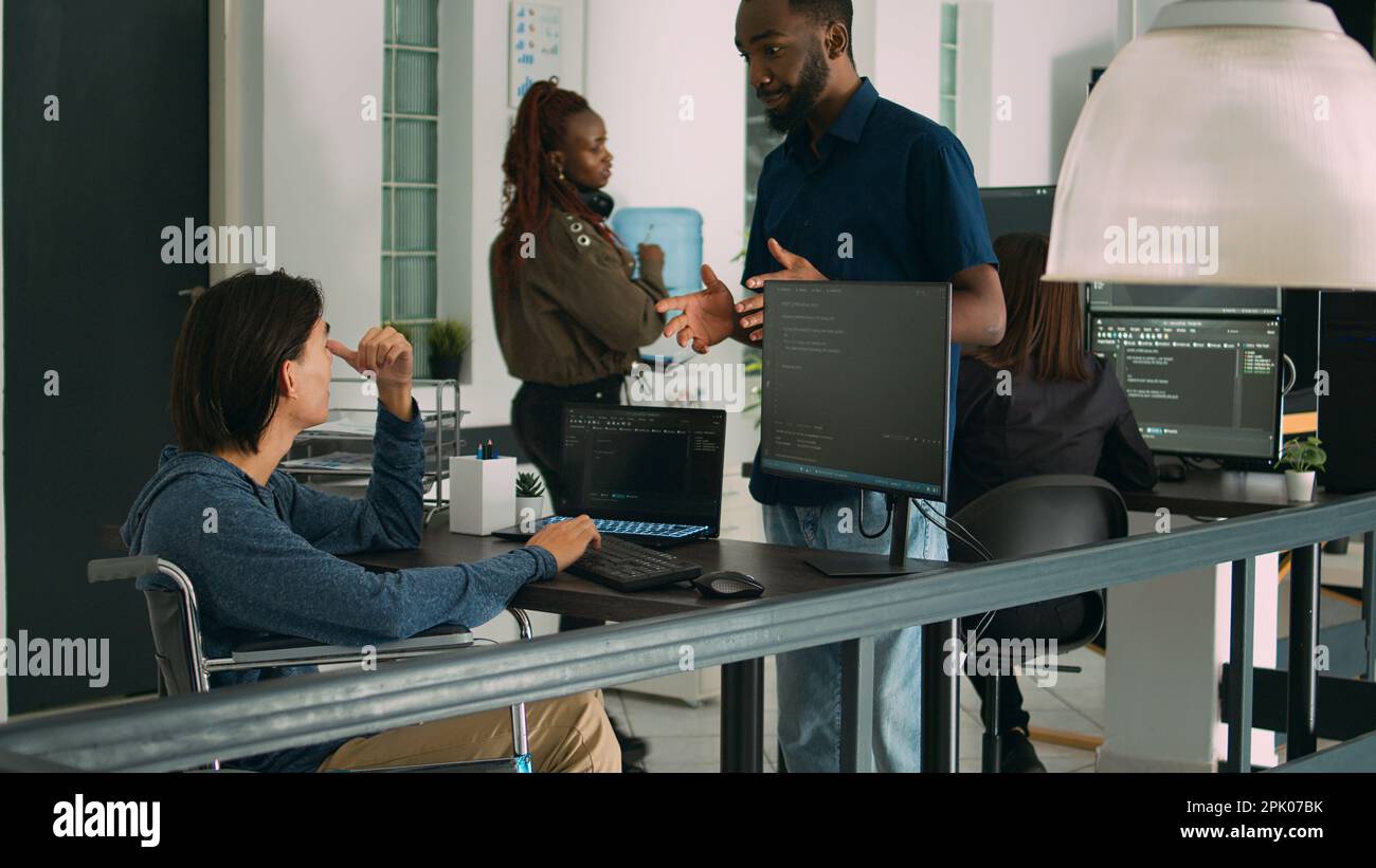 Asian software developer with chronic disability working on server coding, analyzing html language and script on terminal window. Wheelchair user with impairment working on it system. Stock Photo