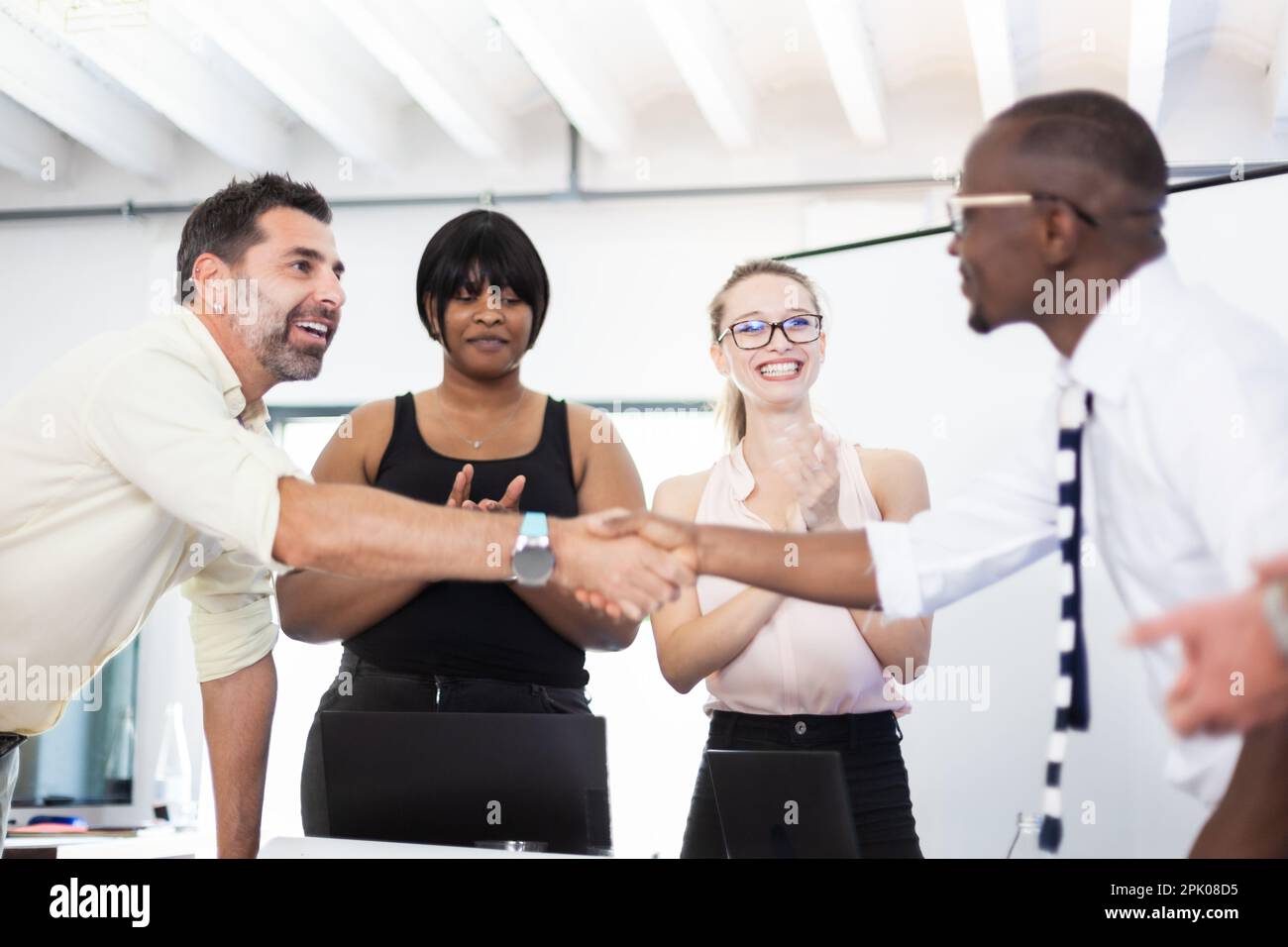 Multiracial business people working together at boardroom table at office. Successful team of colleagues shaking hands and giving applause. Stock Photo
