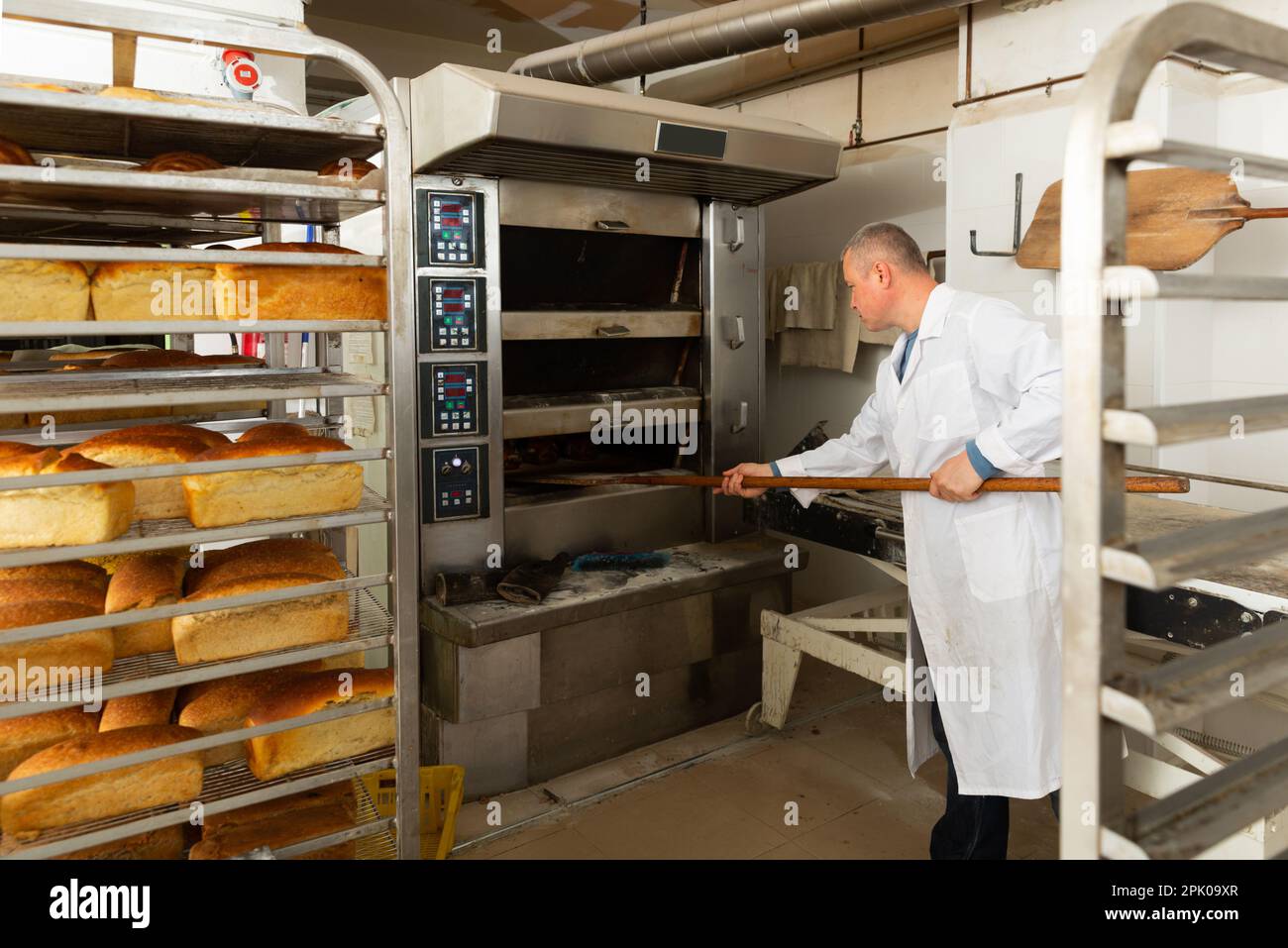 Bakery worker pulling loaves from oven Stock Photo