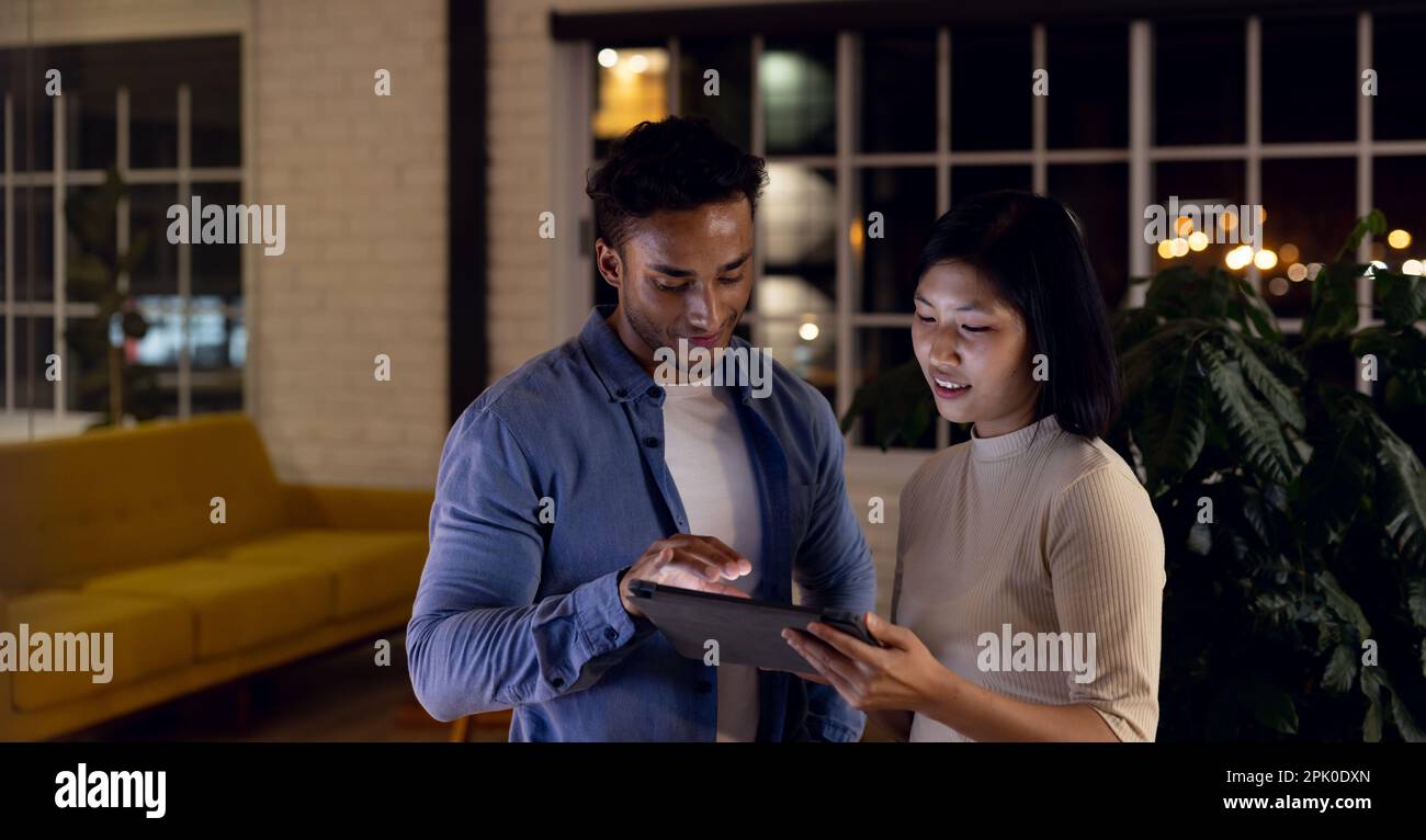 Diverse business people using tablet together and discussing, working late at office Stock Photo