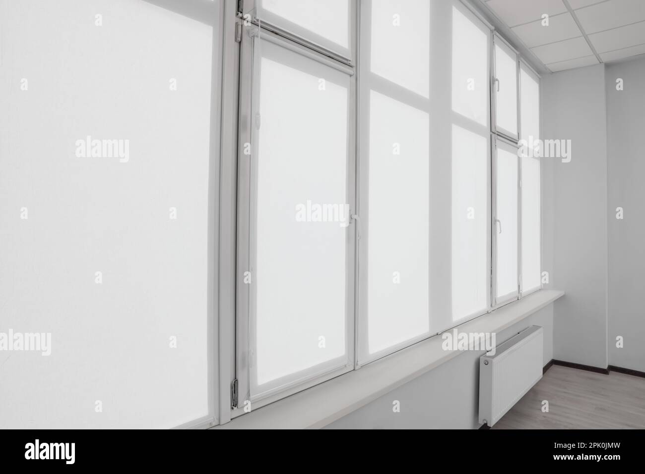Window with closed white roller blinds indoors Stock Photo