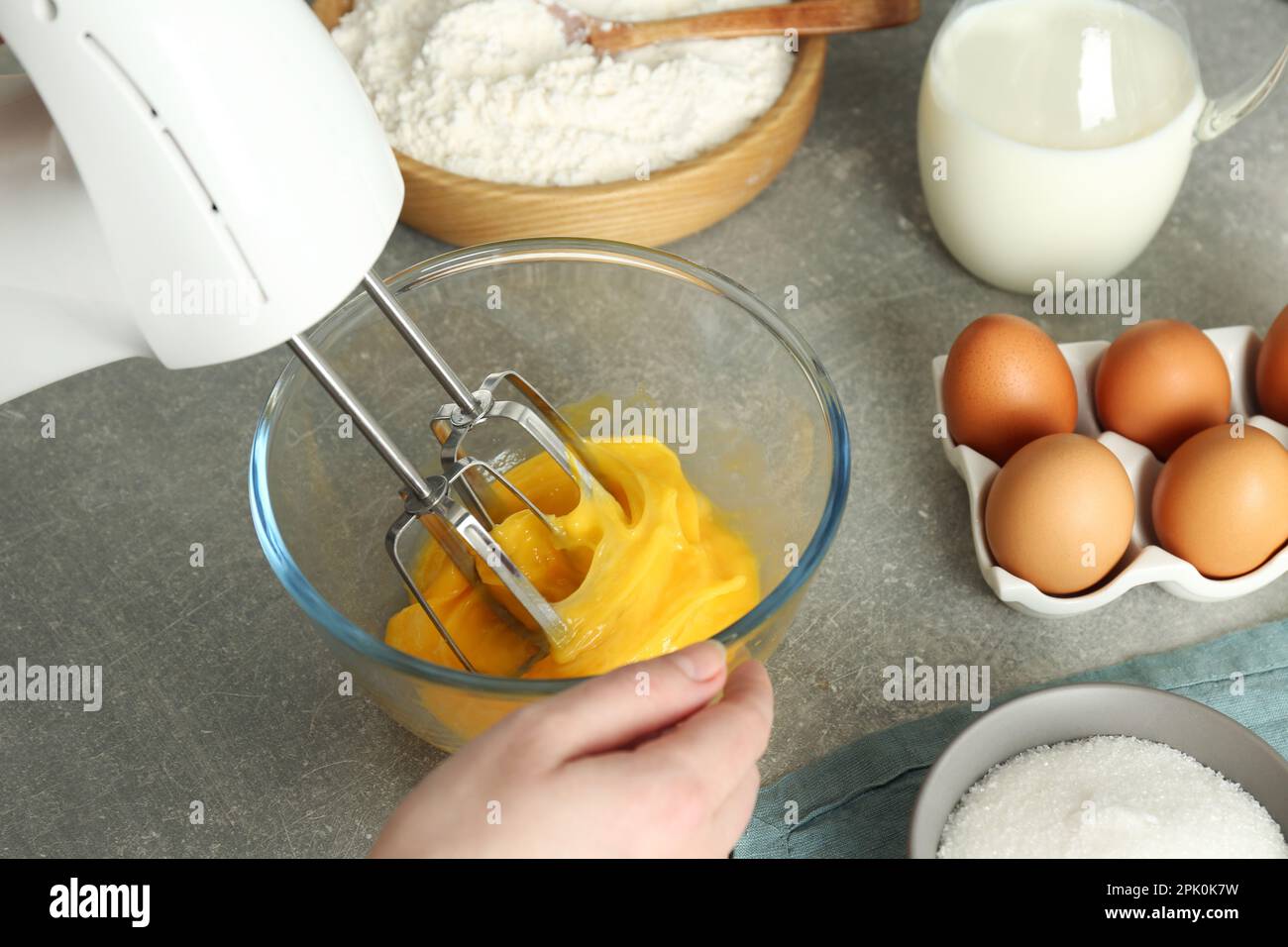 Woman beating eggs with mixer at light grey table, closeup Stock Photo