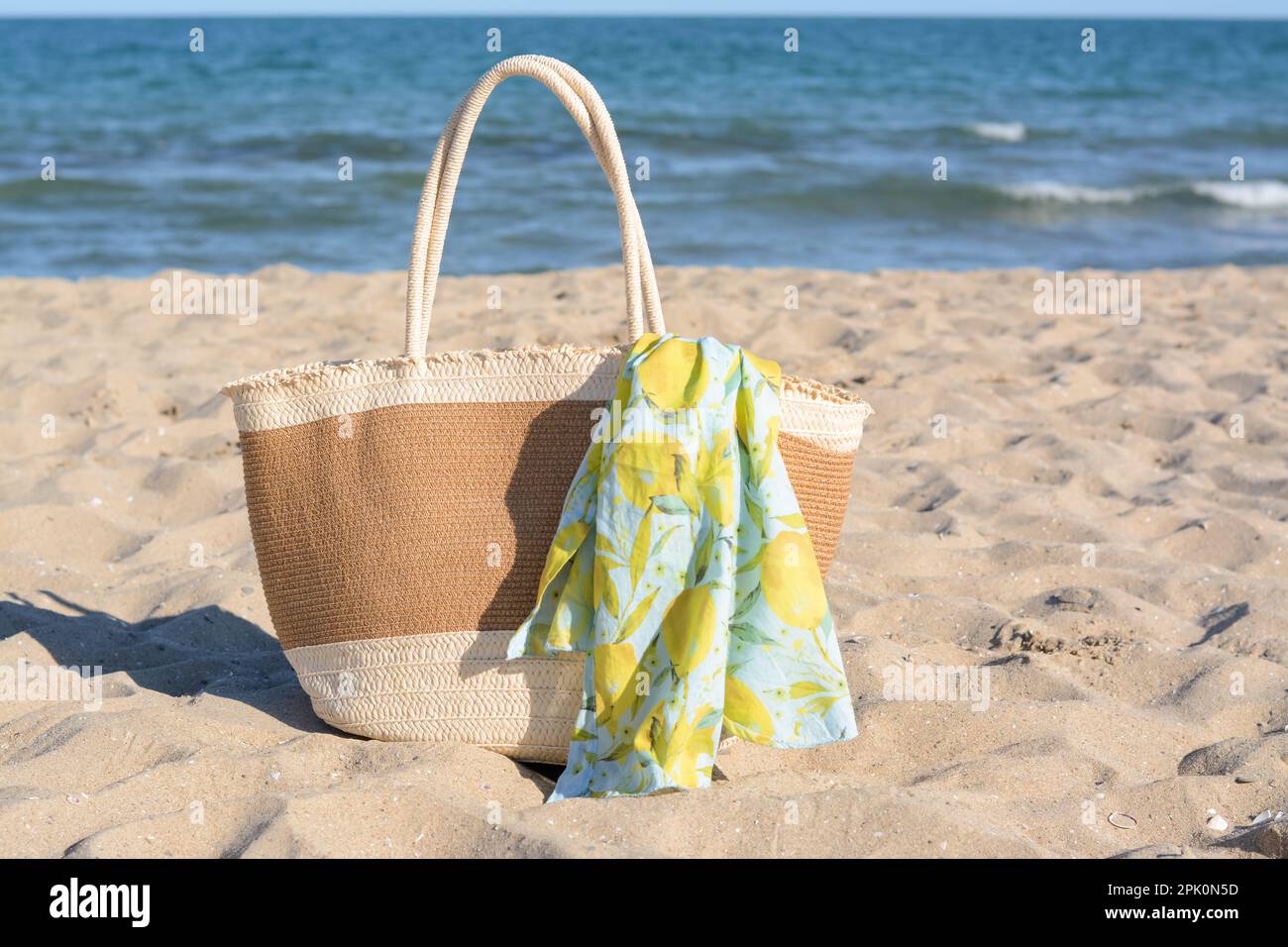 Straw bag with beach wrap on sandy seashore. Summer accessories Stock Photo