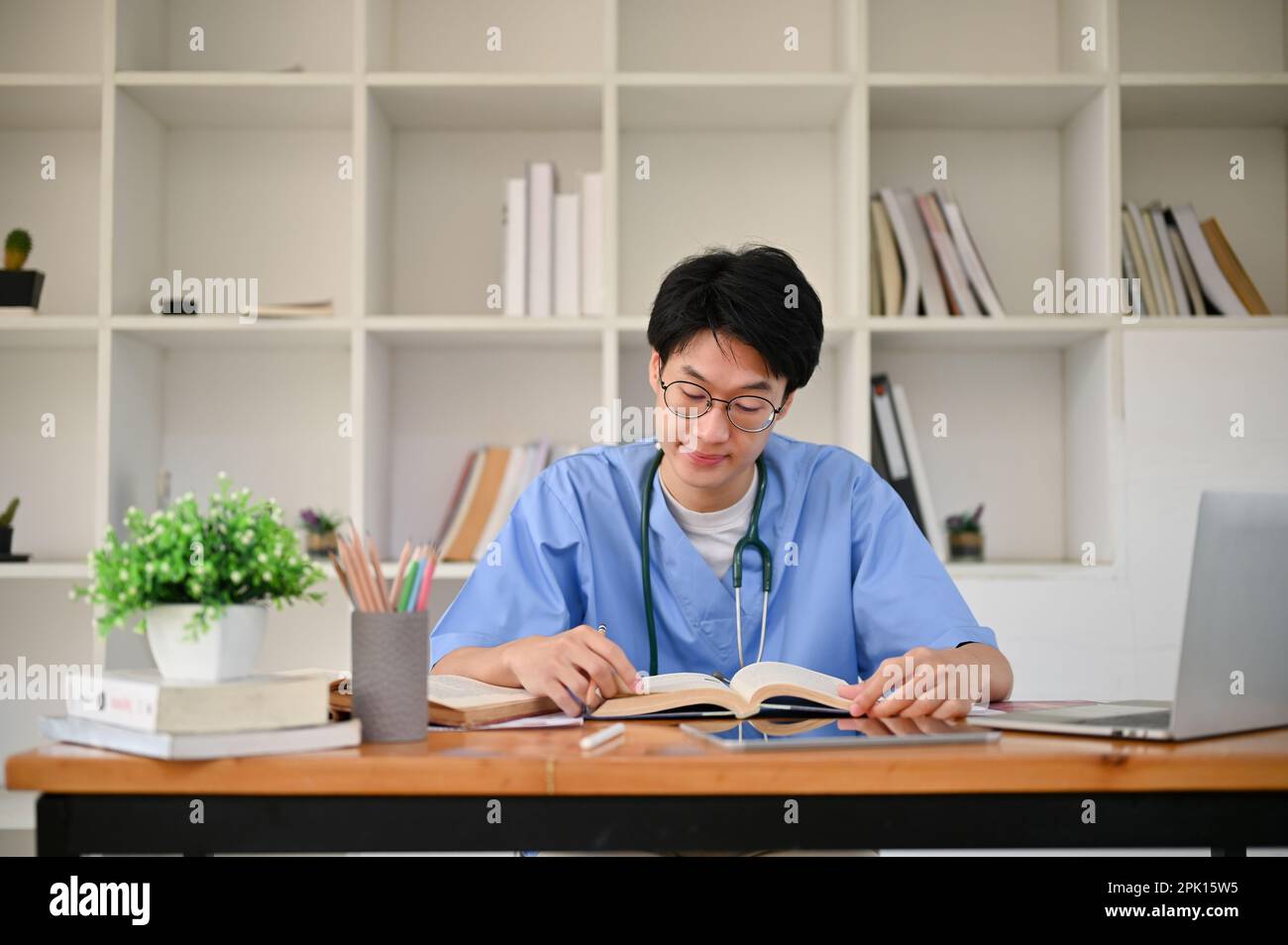 Smart young Asian male medical student in a uniform focuses on reading ...