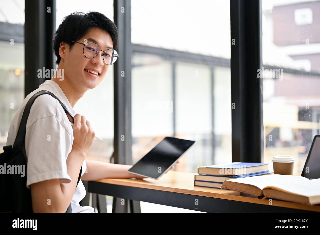 Smart and handsome young Asian male college student wearing glasses sits at a table in a coffee