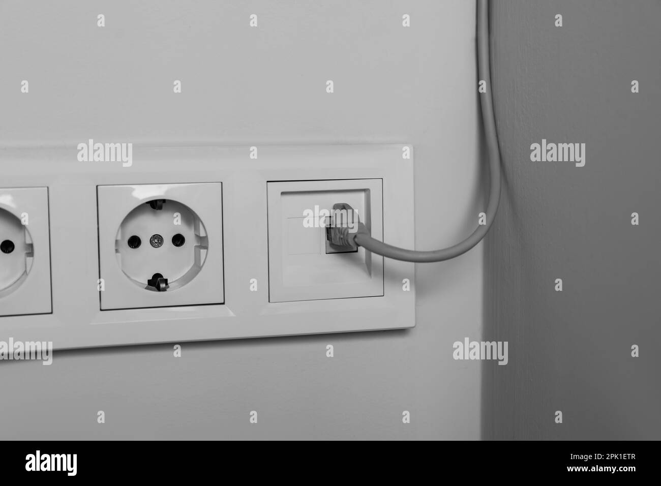 Power sockets with cable on white wall, closeup. Electrical
