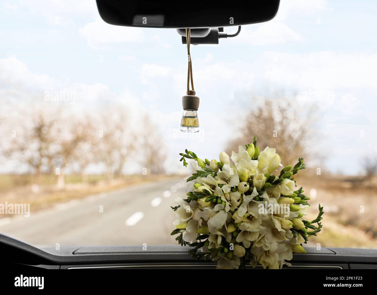 Beautiful bouquet and air freshener hanging on rear view mirror in car