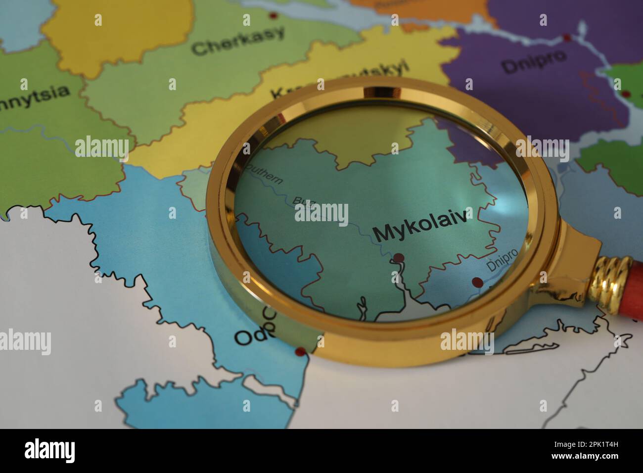 Golden magnifying glass above Mykolaiv region on map of Ukraine, closeup Stock Photo