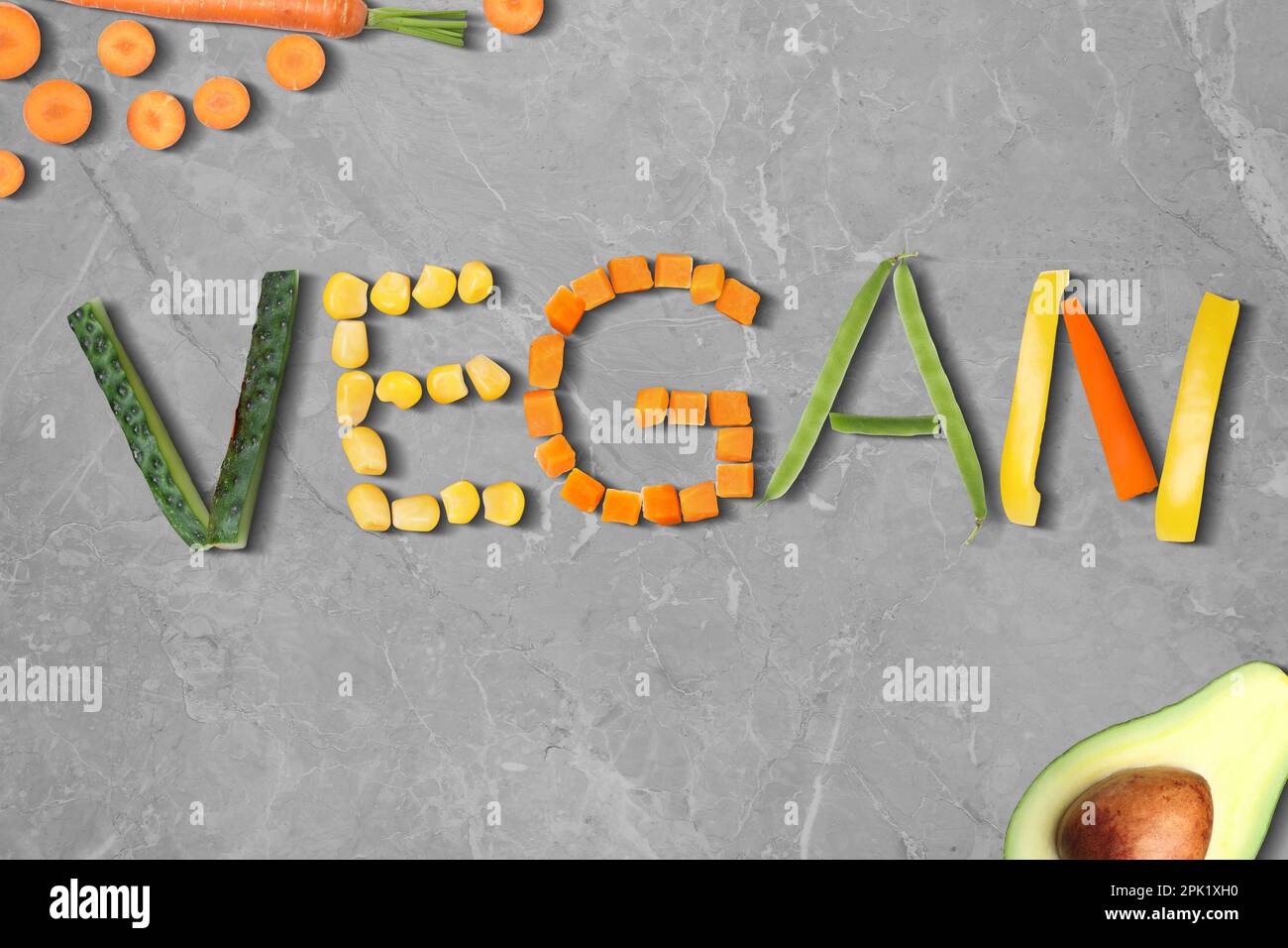 Word VEGAN made of different fresh tasty vegetables on light grey marble background, flat lay Stock Photo