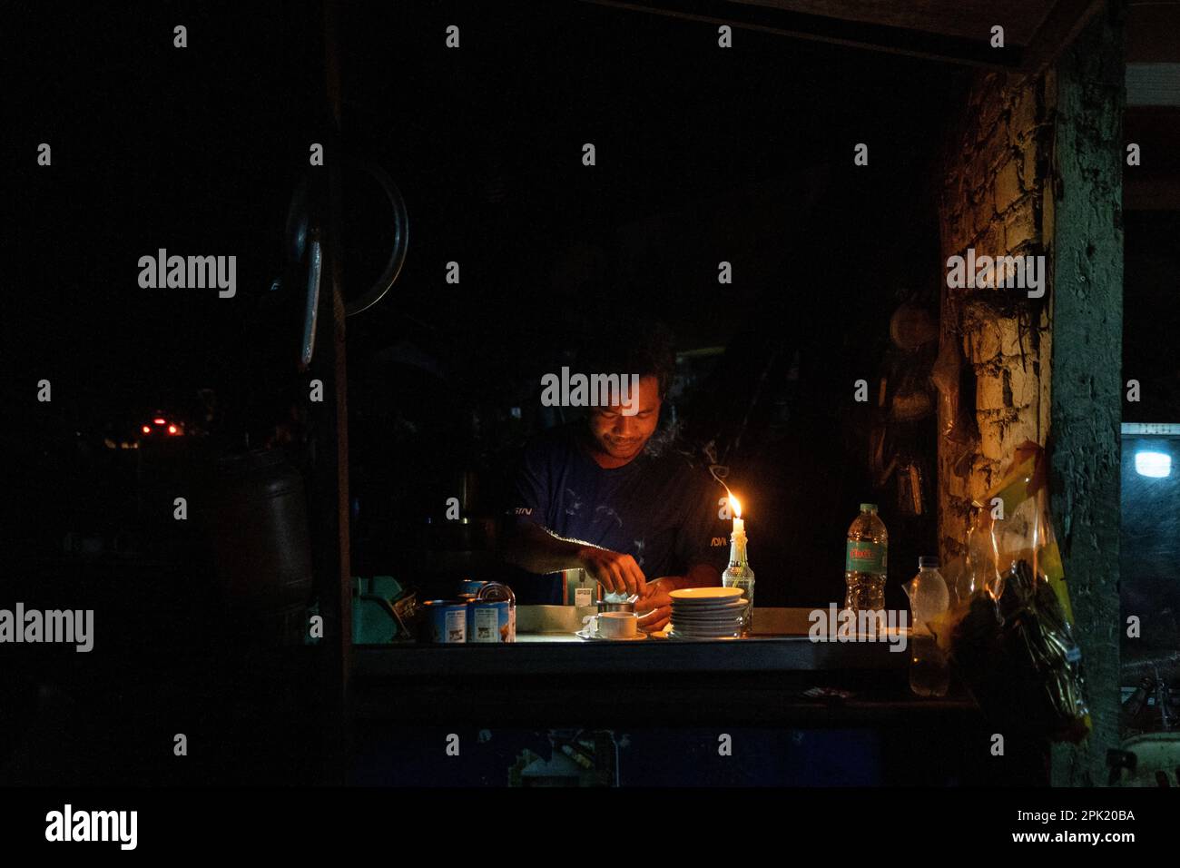 A vendor makes tea by candlelight during a blackout at a shop on the