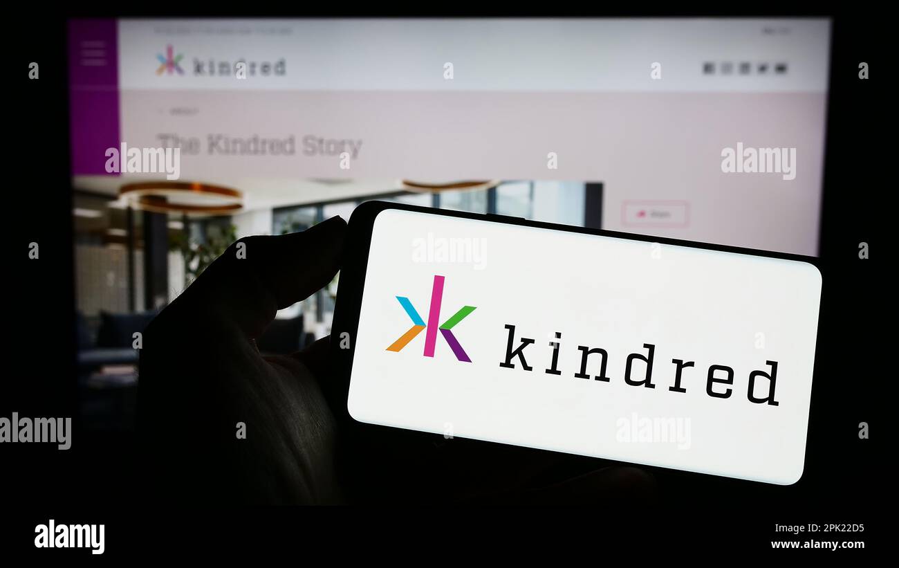 Person holding cellphone with logo of online gambling company Kindred Group plc on screen in front of business webpage. Focus on phone display. Stock Photo
