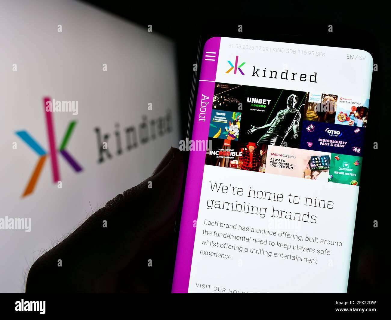 Person holding smartphone with website of online gambling company Kindred Group plc on screen in front of logo. Focus on center of phone display. Stock Photo