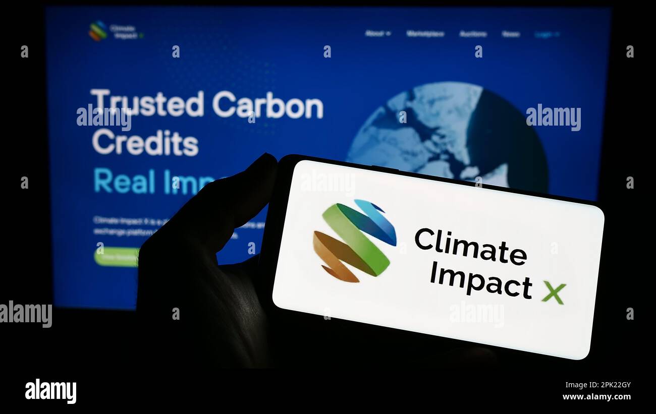 Person holding smartphone with logo of carbon exchange Climate Impact X (CIX) on screen in front of website. Focus on phone display. Stock Photo