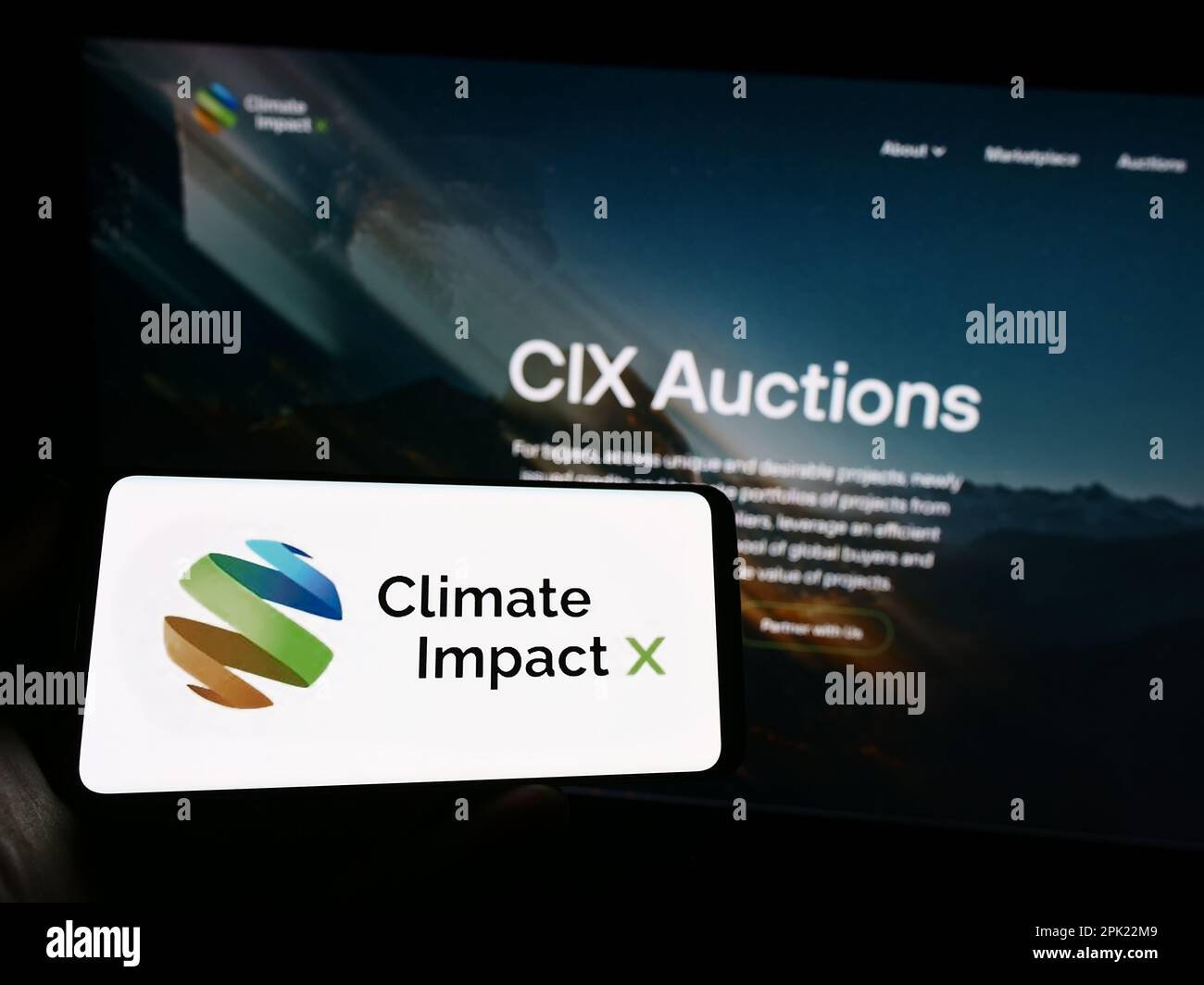 Person holding mobile phone with logo of carbon exchange Climate Impact X (CIX) on screen in front of business web page. Focus on phone display. Stock Photo