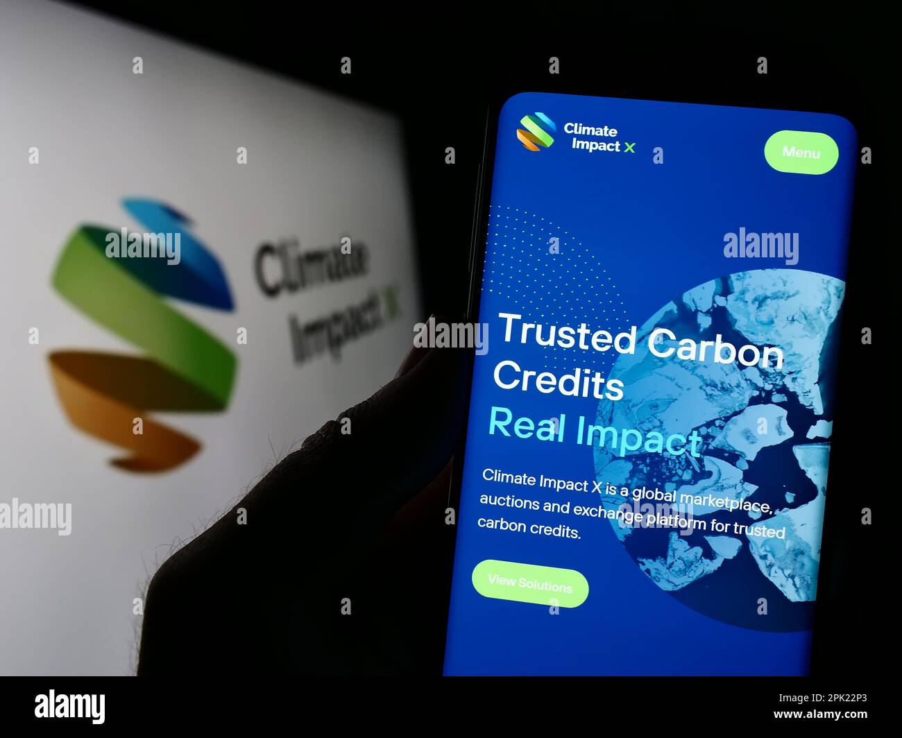 Person holding cellphone with website of carbon exchange Climate Impact X (CIX) on screen in front of logo. Focus on center of phone display. Stock Photo