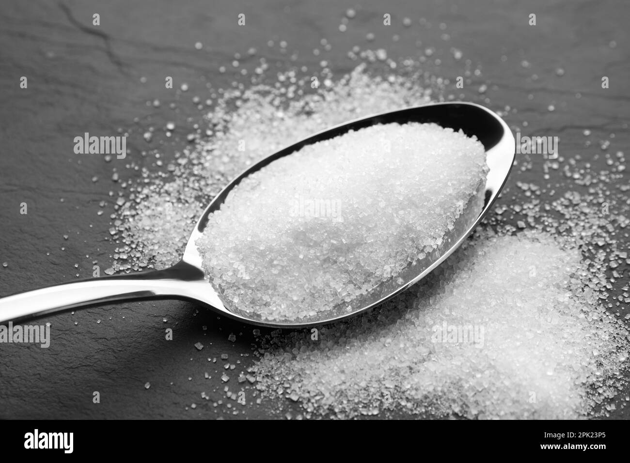 Granulated sugar and spoon on black table, closeup Stock Photo