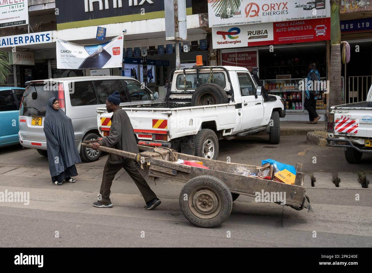 Arusha, Tanzania - October 17th, 2022: A porter pulling a wooden cart in a main street of Arusha, Tanzania. Stock Photo