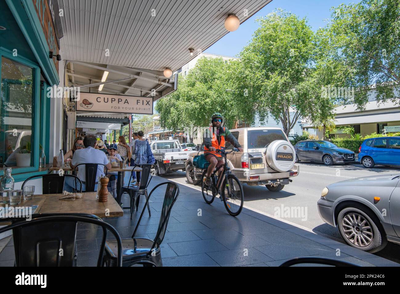 People dining alfresco style on the footpath (sidewalk) while a Uber food delivery bicycle rider rides past in Glebe, New South Wales, Australia Stock Photo