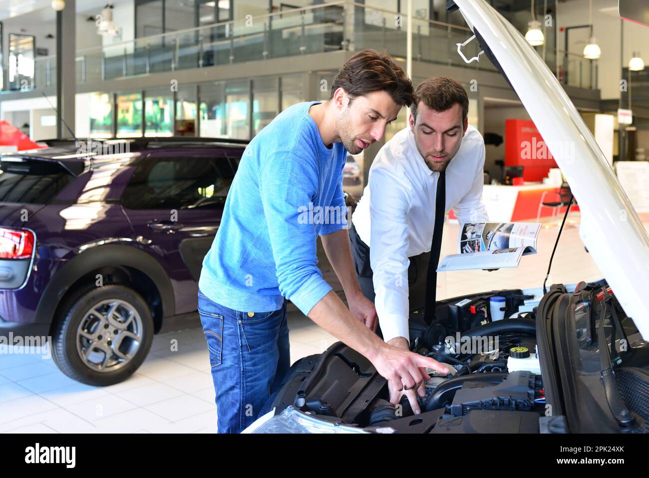 Advice in the car dealership seller and young man selling a new car