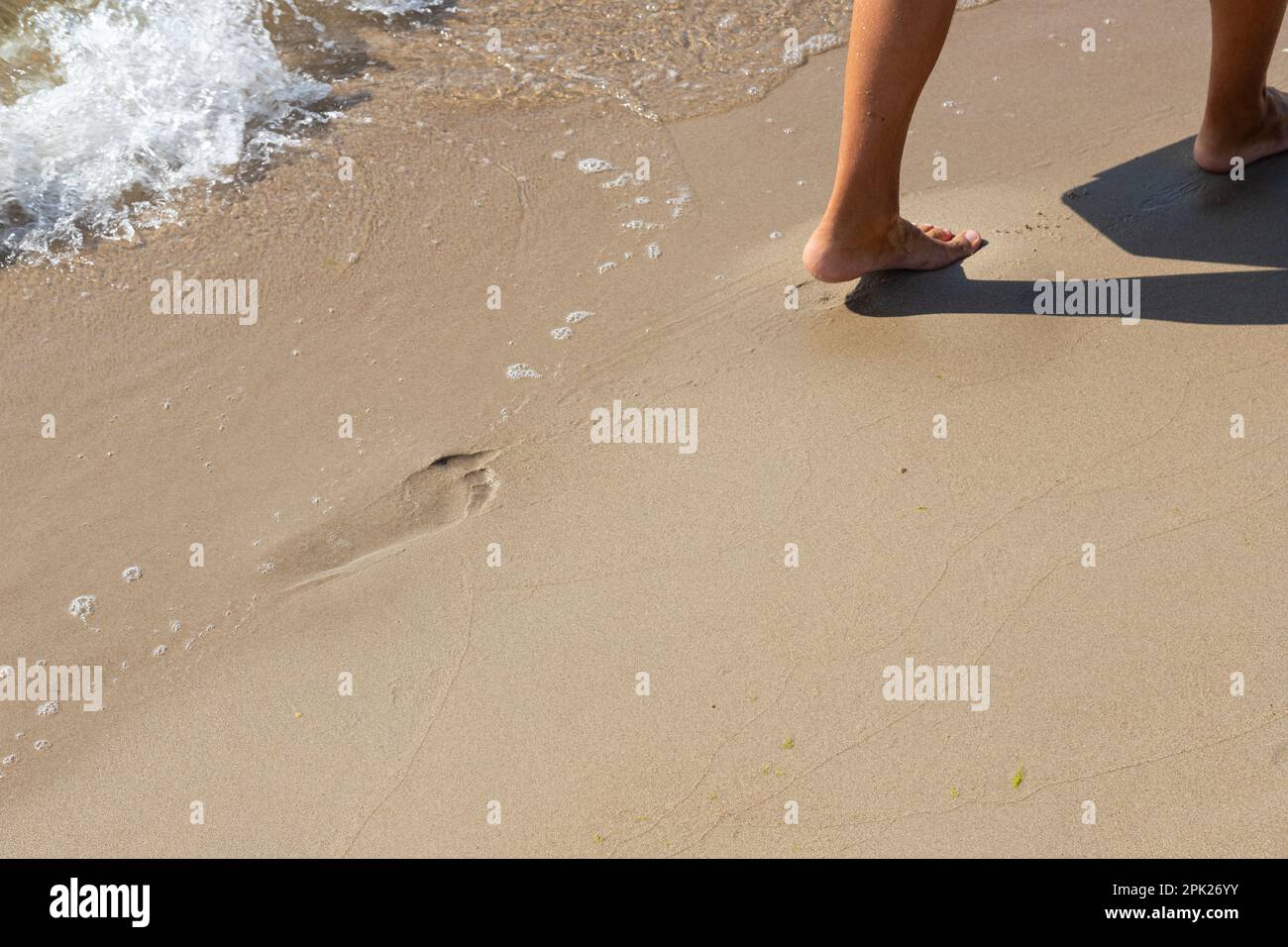 Footprints of a man on the yellow beach sand from walking barefoot by the sea with water that washes away the footprints. Contemplation of life Stock Photo