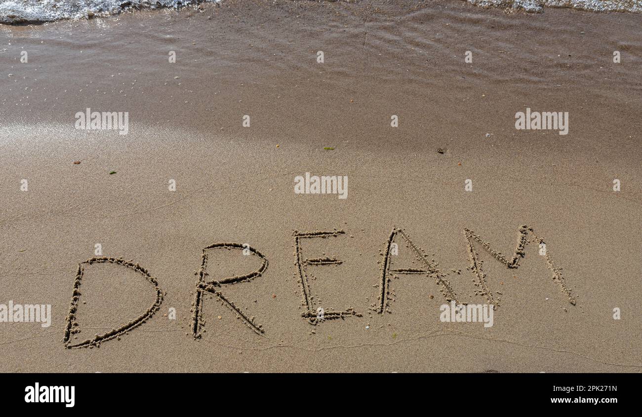 the inscription DREAM on the sand of the coastline. Stock Photo