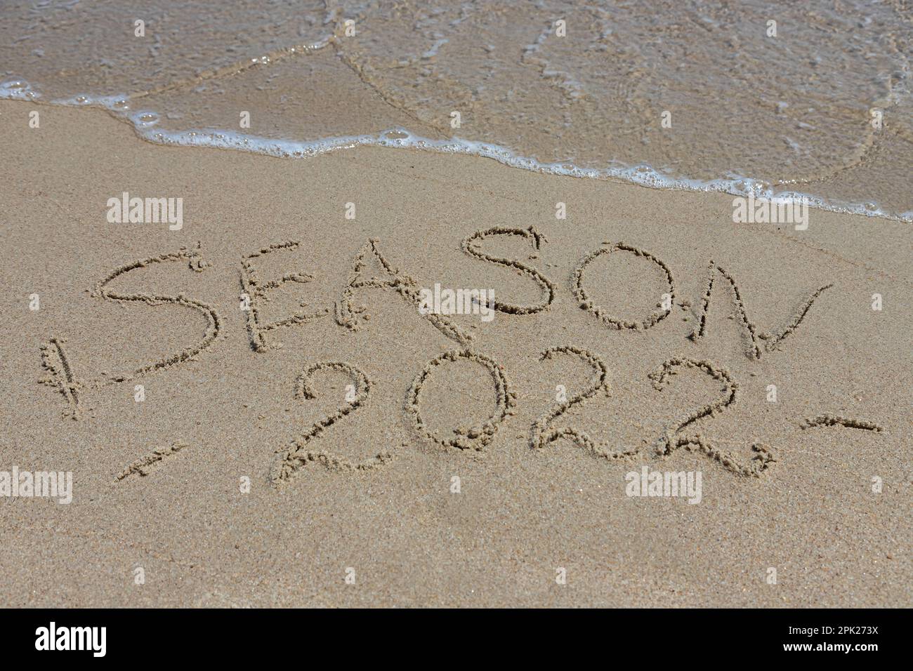 The inscription season 2022 on the sand by the water and the rising wave, seashore beach vacation by the sea. Stock Photo