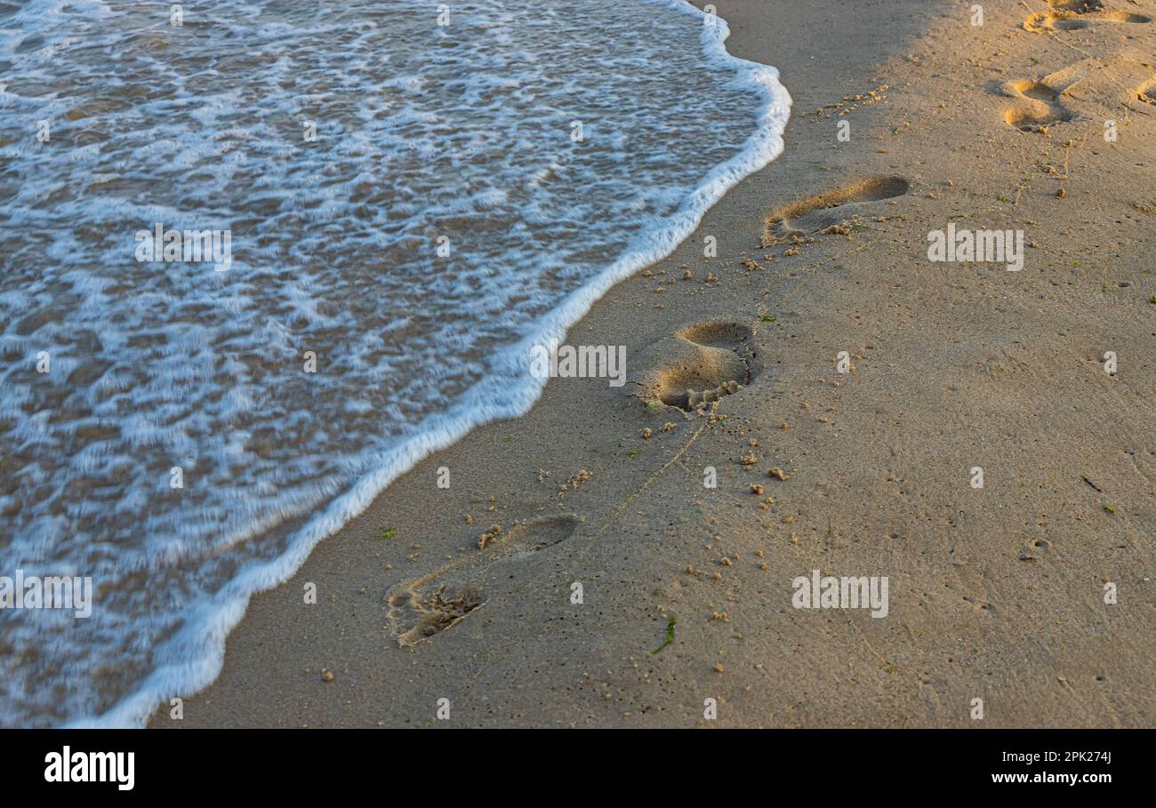 Footprints of a man on the yellow beach sand from walking barefoot by the sea with water that washes away the footprints. Contemplation of life Stock Photo