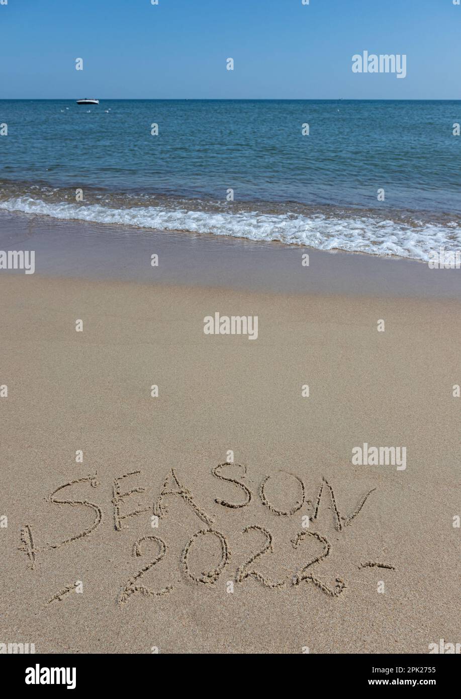 The inscription season 2022 on the sand by the water and the rising wave, seashore beach vacation by the sea. Stock Photo