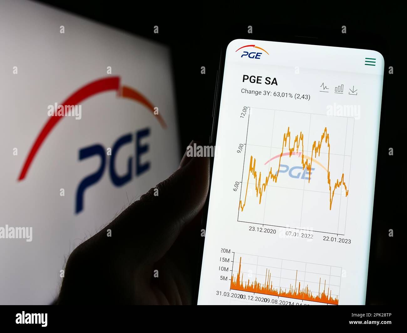 Person holding cellphone with webpage of company PGE Polska Grupa Energetyczna S.A. on screen in front of logo. Focus on center of phone display. Stock Photo