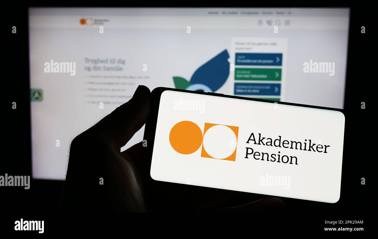 Person holding smartphone with logo of Danish pension fund AkademikerPension on screen in front of website. Focus on phone display. Stock Photo