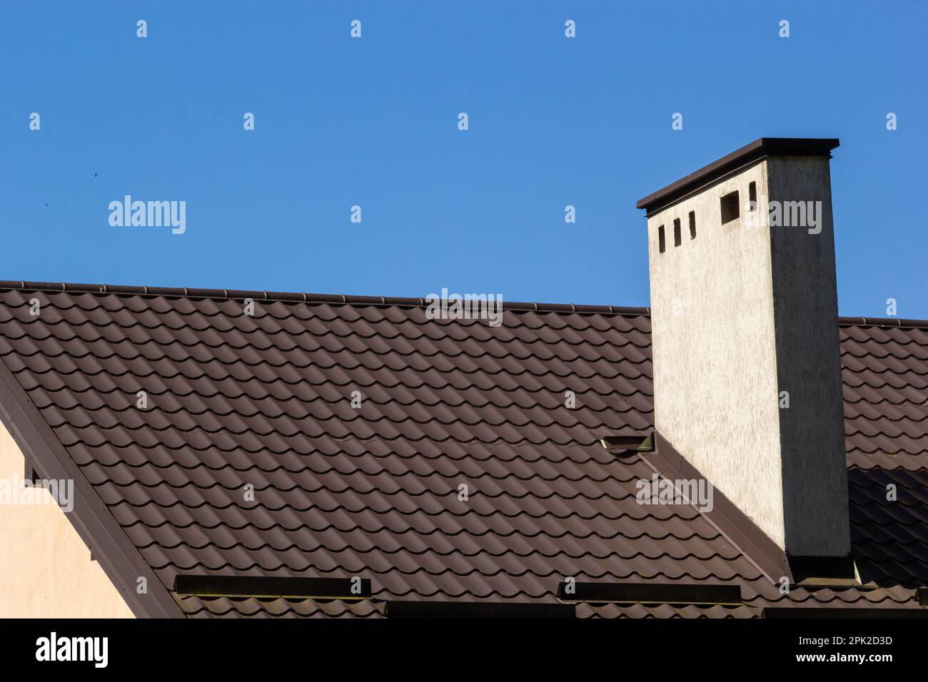 Roof of a new home. Ceramic chimney, metal roof tiles, gutters, roof window. Single family house. Stock Photo