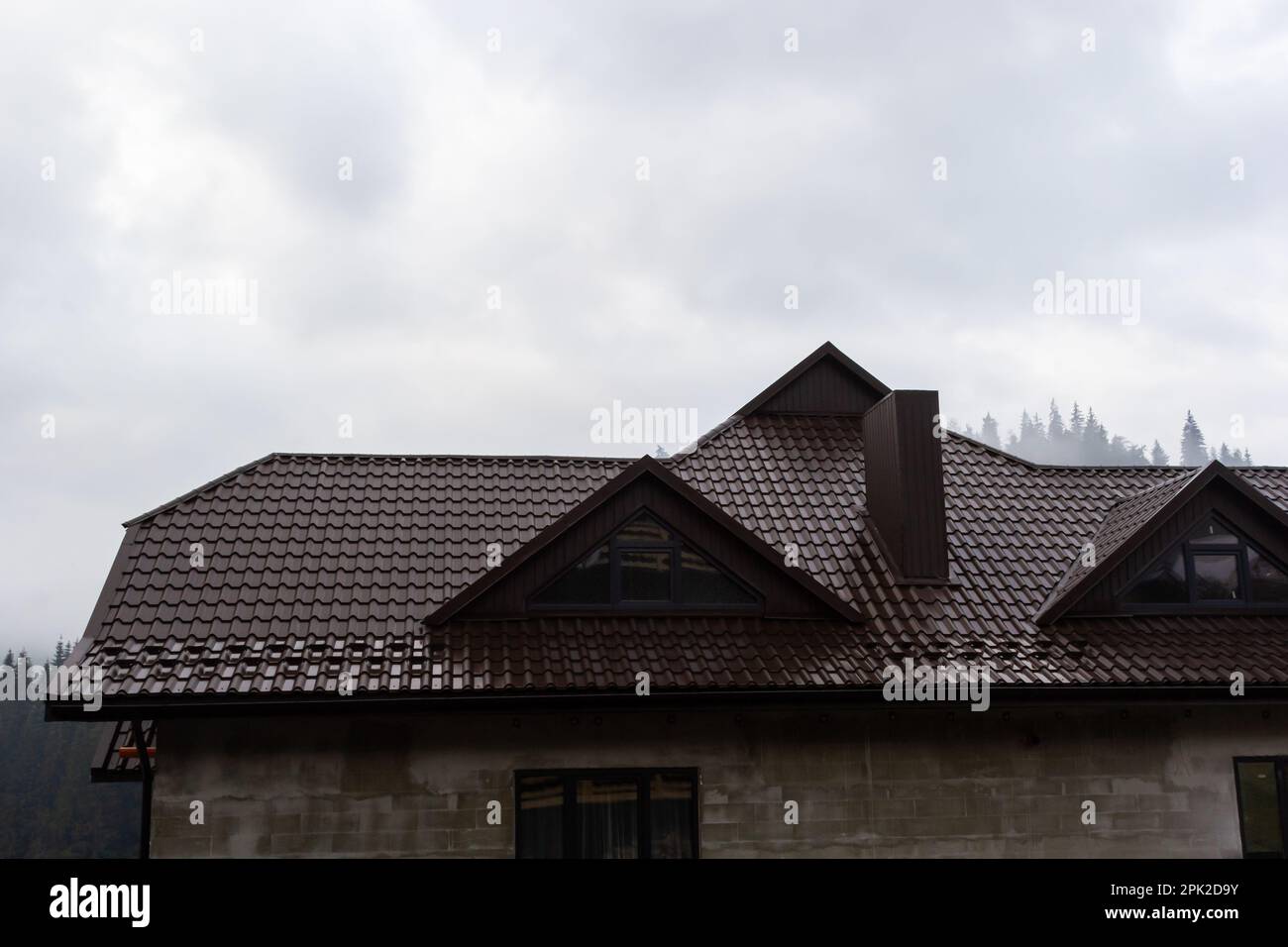 House with new brown metal tile roof and rain gutter. Metallic