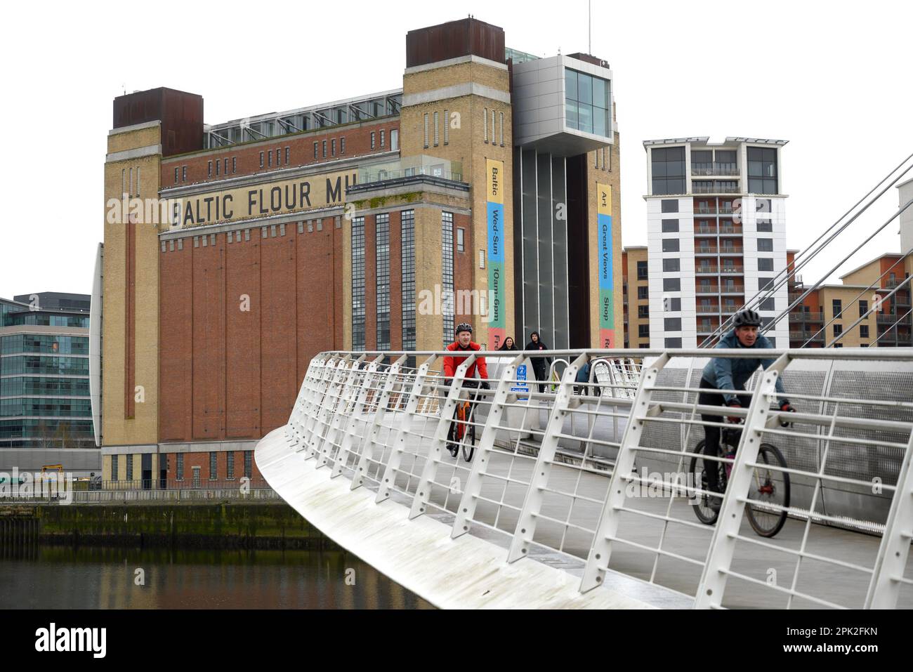 Gateshead, Tyne and Wear, England, UK. Baltic Centre for Contemporary Art seen from the Gateshead Millennium Bridge of the river Tyne - two men cyclin Stock Photo