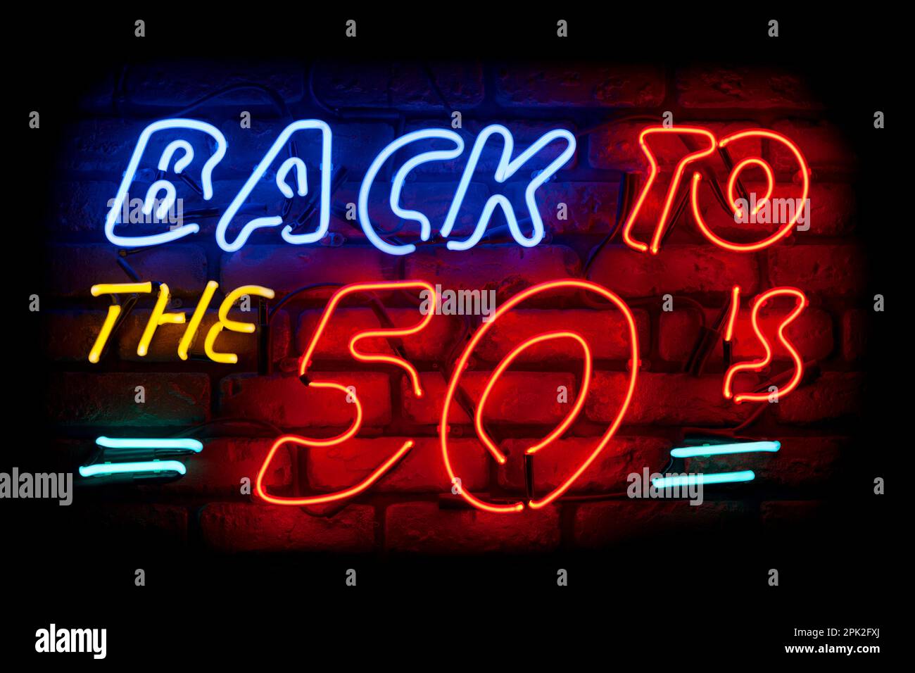 Neon light on a brick wall saying; Back to the 50's. Stock Photo