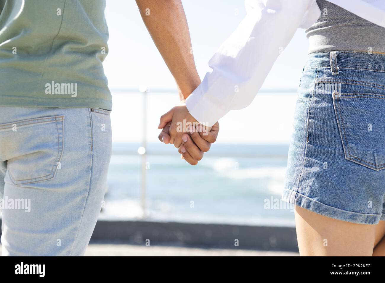 Midsection of diverse couple holding hands on promenade by the sea Stock Photo