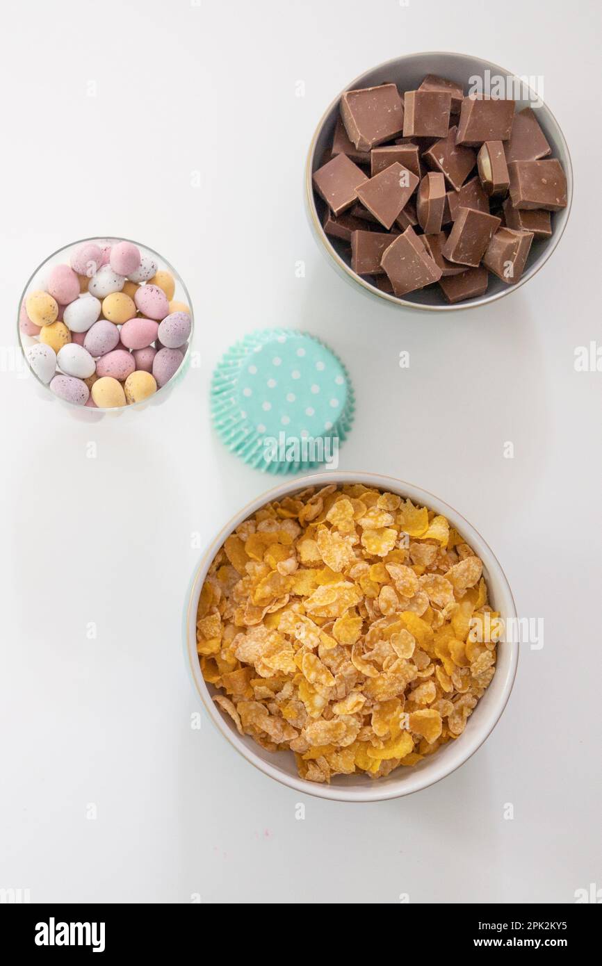 Ingredients in bowls for making chocolate nests - cornflakes, chocolate chunks, mini eggs and cupcake cases (Easter) Stock Photo
