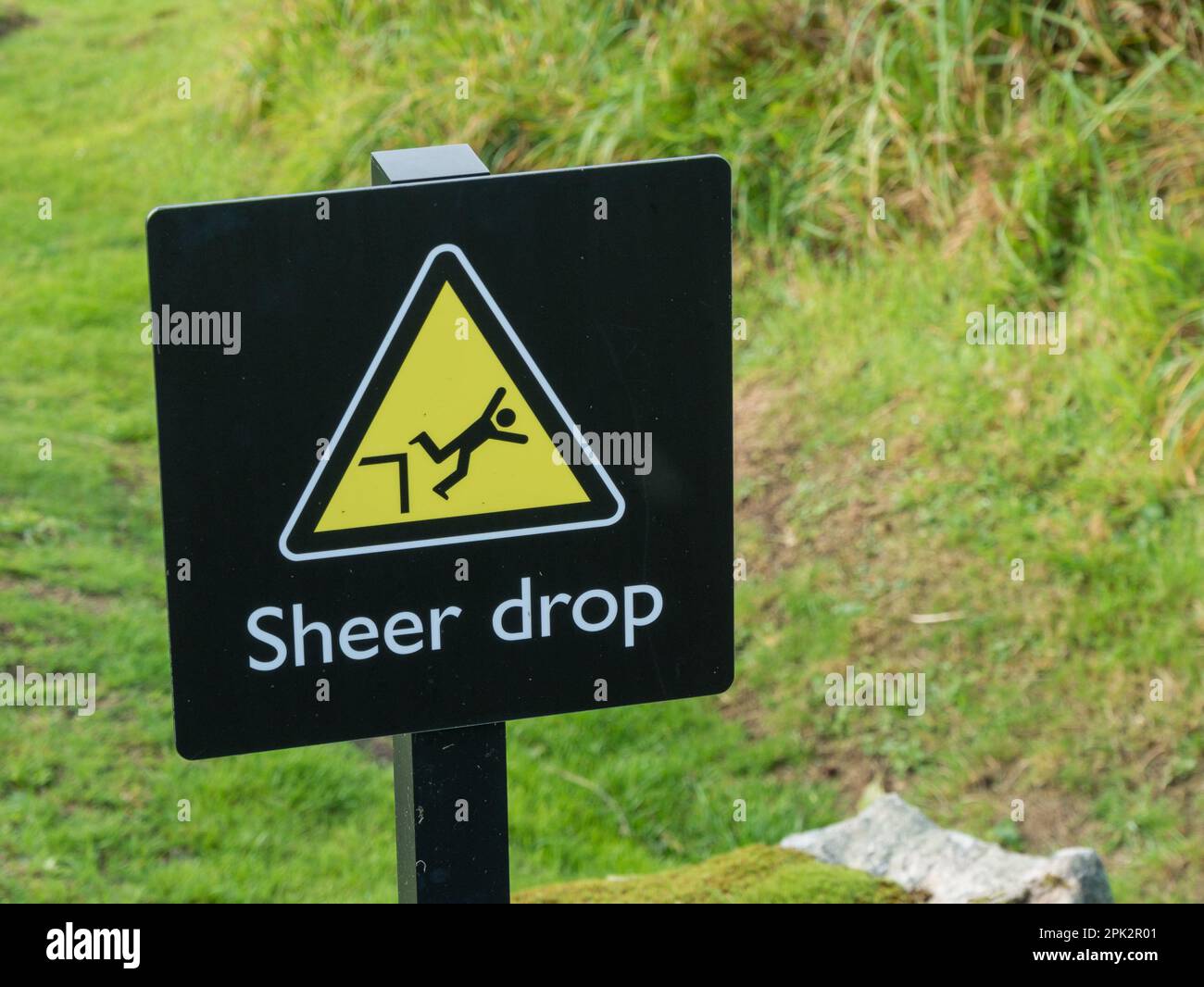 Danger 'Sheer drop' warning sign with man falling graphic in yellow warning triangle with English language text below Stock Photo