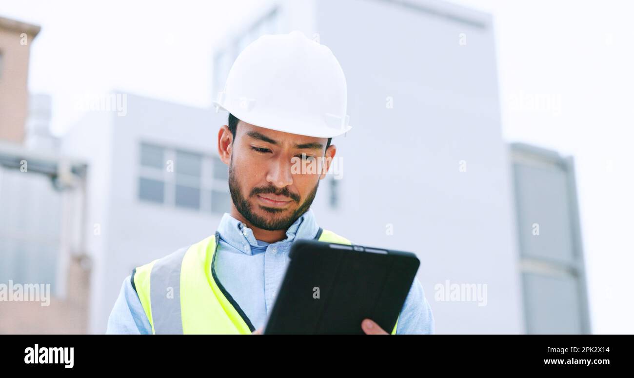 Construction worker holding a digital tablet while doing inspection. Organized male engineer or technician in a hardhat checking project plan with Stock Photo