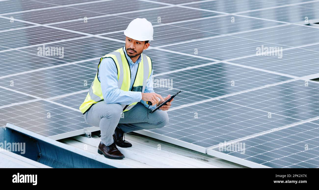 Young engineer or contractor inspecting solar panels on a roof in the city. One confident young manager or maintenance worker smiling while installing Stock Photo