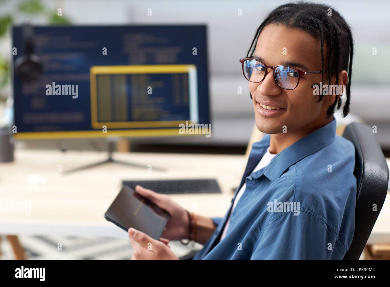 Portrait of smiling computer programmer holding tablet and looking at camera at workplace Stock Photo