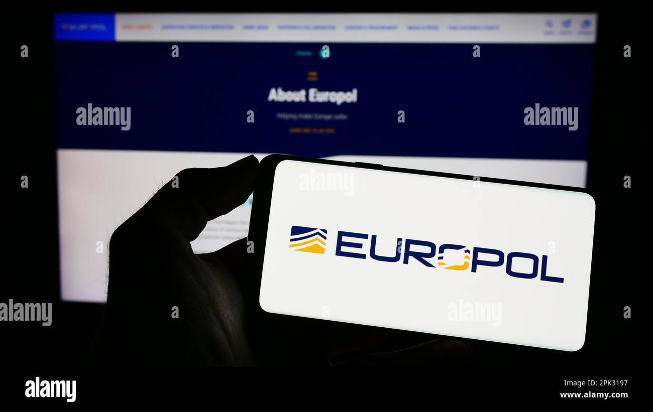 Person holding cellphone with logo of EU law enforcement agency Europol on screen in front of webpage. Focus on phone display. Stock Photo