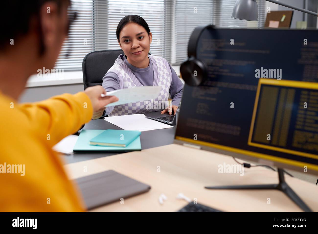 Portrait of two young people working in IT development office and handing documents across table while writing code Stock Photo