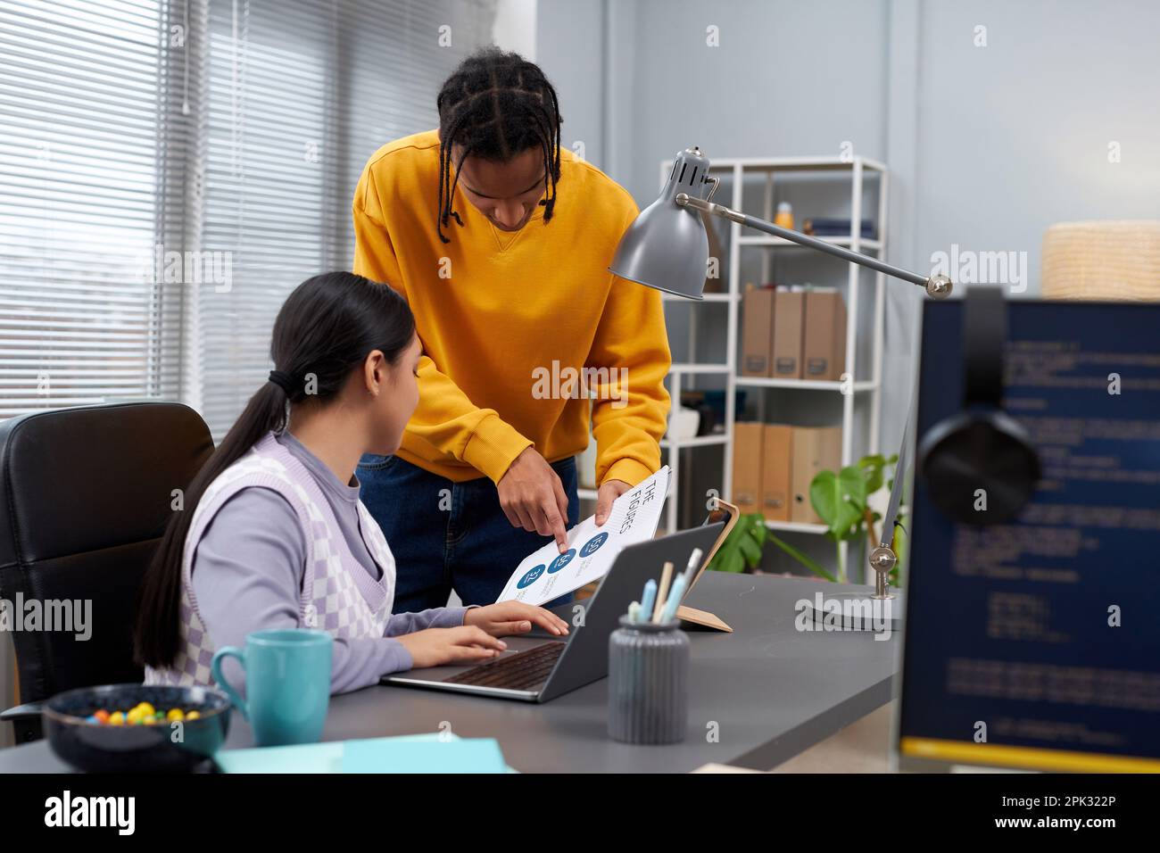Portrait of two young people discussing document while collaborating on project in IT development office Stock Photo