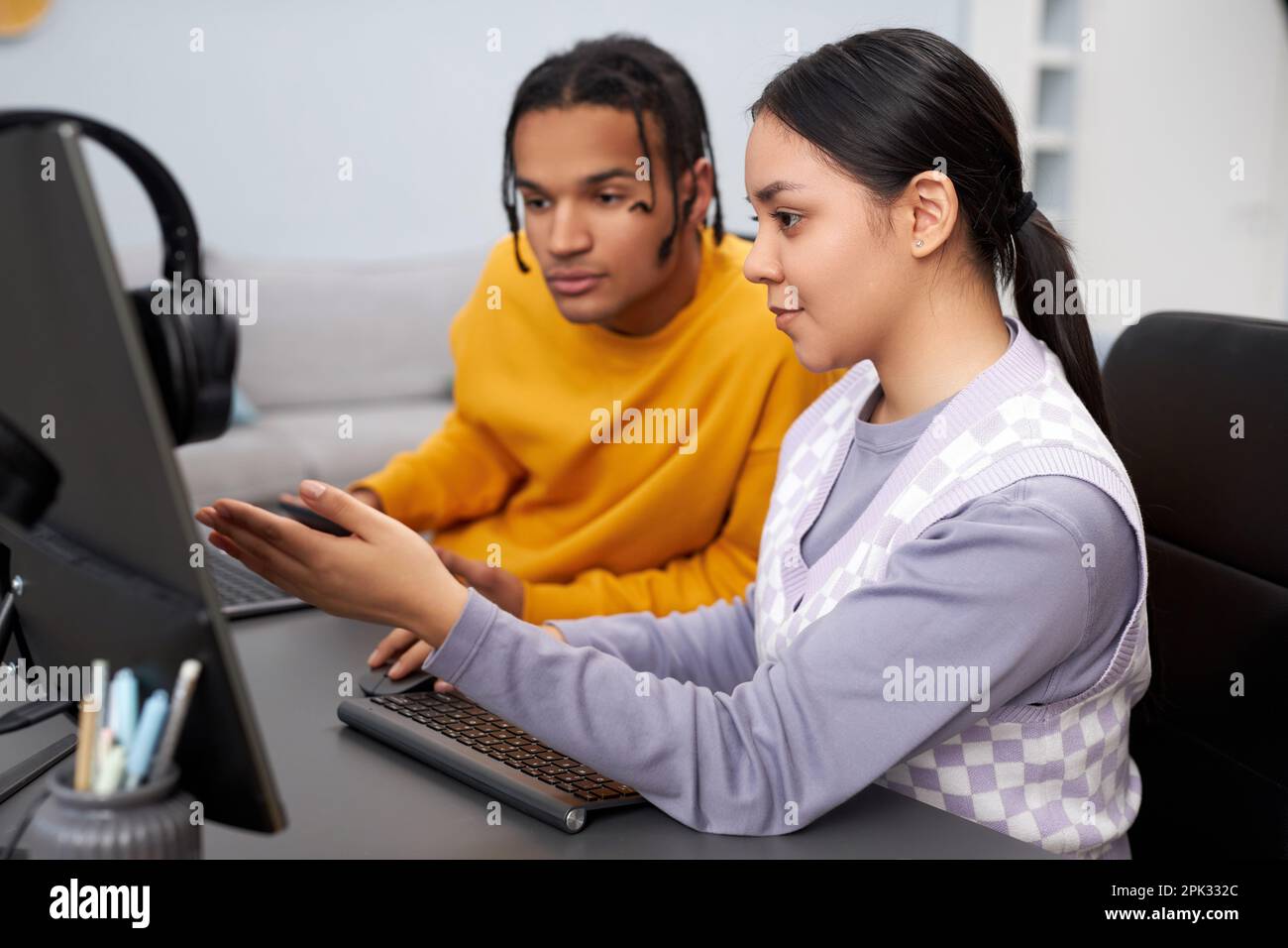 Two young people writing code in office with focus on multiethnic woman pointing at computer screen Stock Photo