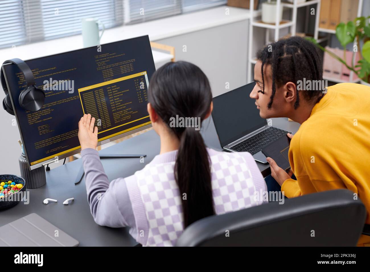 High angle view of two young people writing code in office and pointing at computer screen Stock Photo