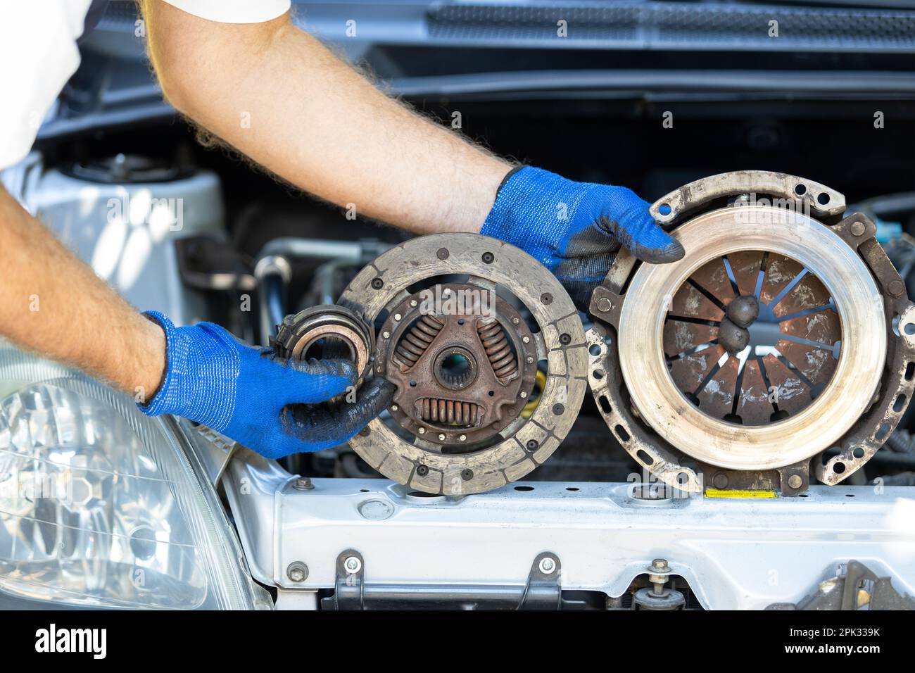 Automotive worker holding used car clutch disc, pressure plate and release  bearing in front of the vehicle engine Stock Photo - Alamy